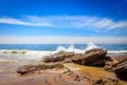 Crashing waves over rocky shores under a bright blue sky at Laguna Beach, CA.